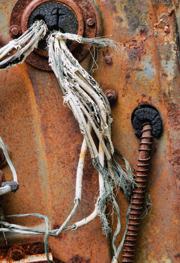 Frayed and damaged electrical wiring on a rusted metal surface, showing exposed wires that need replacement.